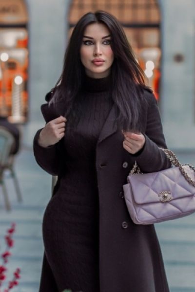 A picture of a very good looking brunette lady wearing a big coat 
