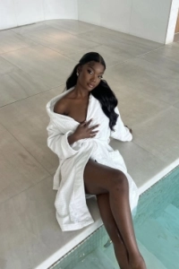 A sexy ebony escort sat by a pool in her robe 