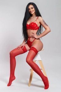 Slim busty brunette escort wearing red latex 