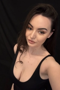 A brunette escort wearing a low cut black top 