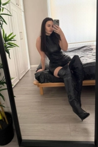 Mistress Janey is sitting on a black sheet on her bed 
