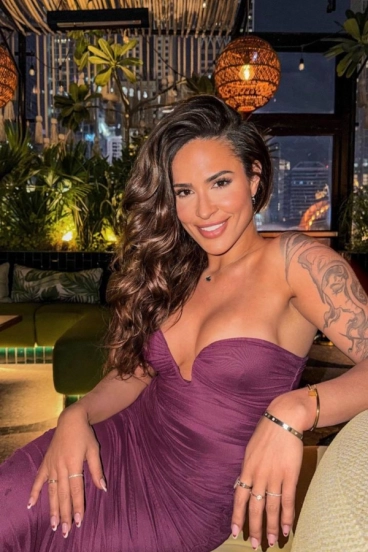 Samantha seated in a purple strapless dress at a restaurant with hanging lantern lights