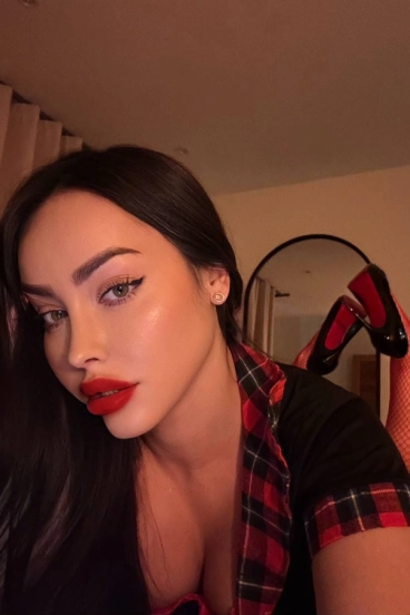 Vanessa Lux takes a playful selfie in a red and black checked outfit with heels raised behind her.