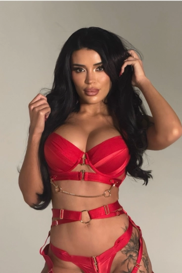 Tornia in red strappy lingerie with gold chain details and long black hair.