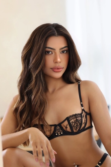 Mannu in a close-up portrait wearing delicate black lace lingerie with long wavy brunette hair.