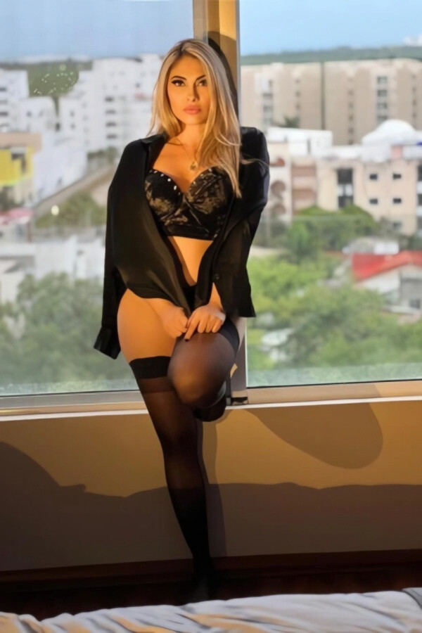 Sensual blonde Brazilian escort in lingerie by window