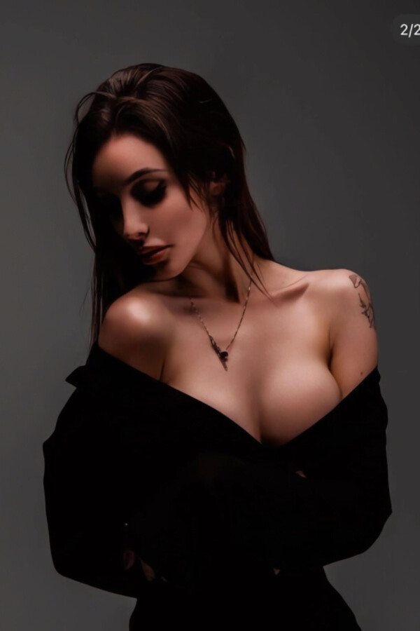 Rafaela with an off-shoulder black shirt in a low-light portrait