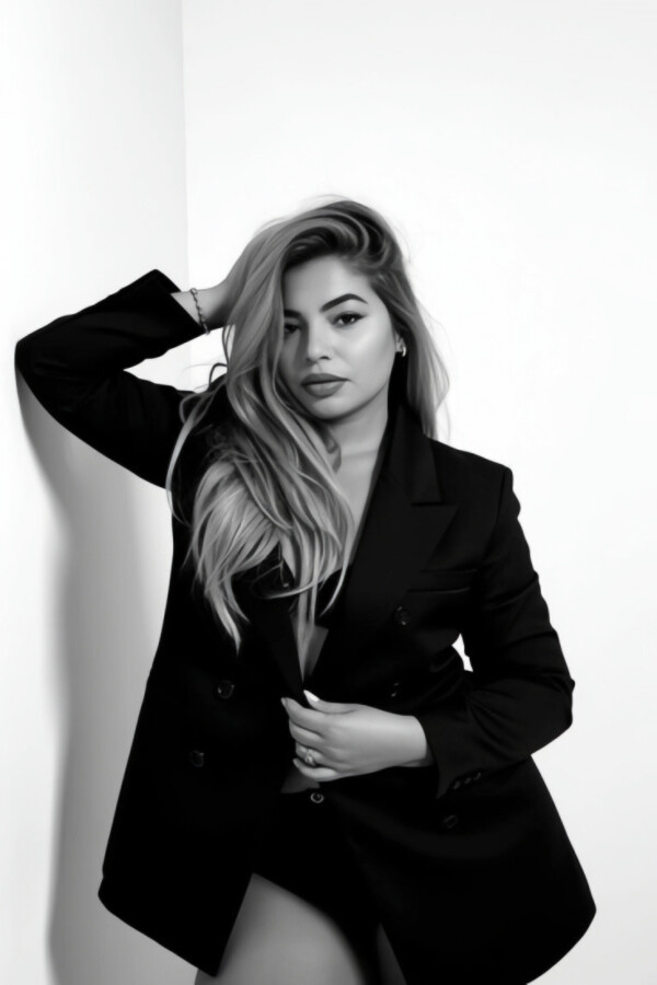Charitie in a black blazer posing against a white wall