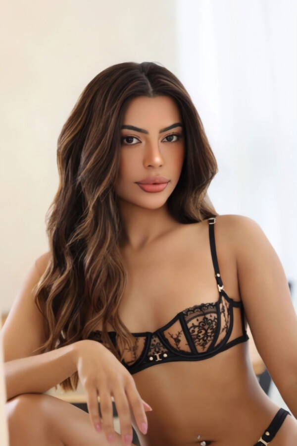 Mannu in a close-up portrait wearing delicate black lace lingerie with long wavy brunette hair.