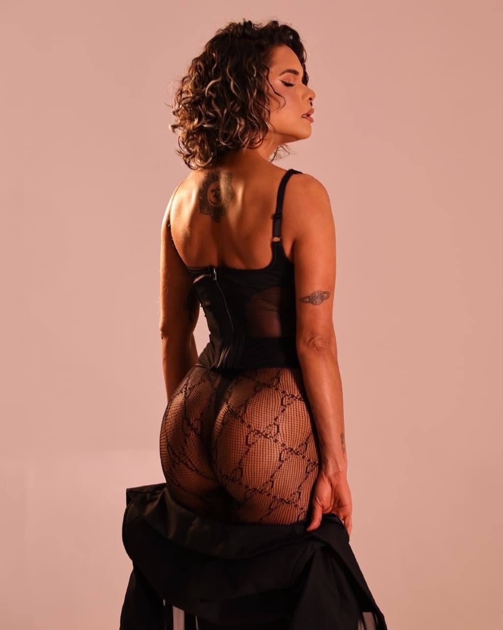 Estebana poses from behind in a black bodysuit and patterned fishnet tights.
