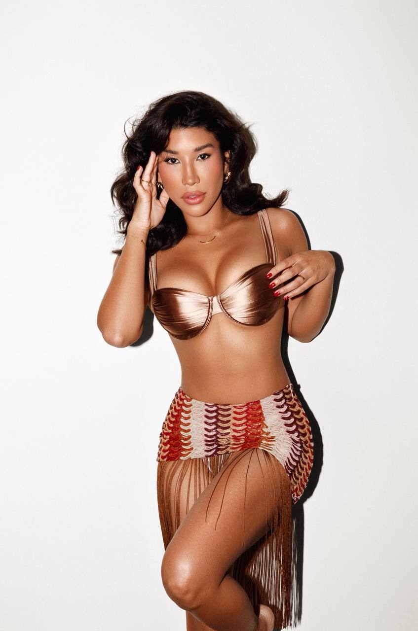 Marley poses against a white wall in a bronze satin top and fringed patterned skirt.