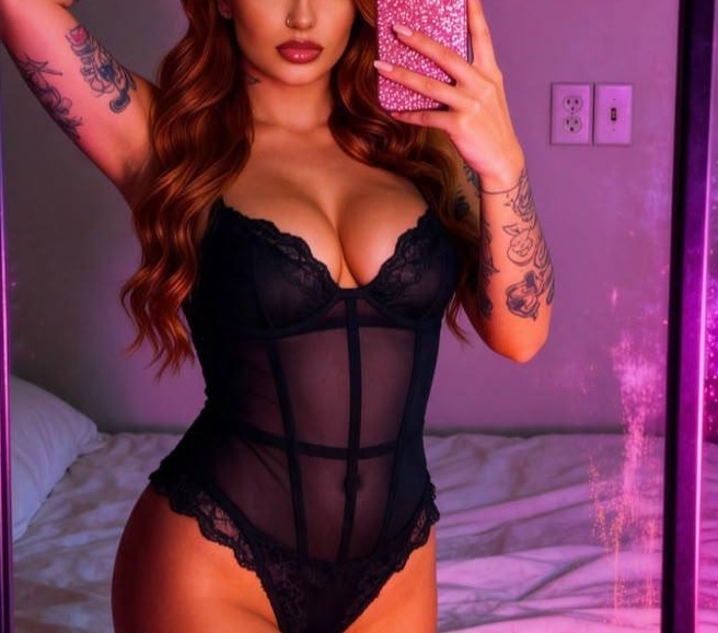 Estelle takes a mirror selfie in a sheer black lace bodysuit under pink lighting.