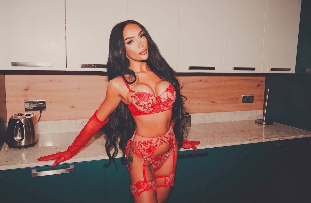 Jess posing in red embroidered lingerie and matching sheer gloves in a modern kitchen